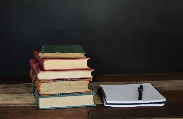 A pile of books next to a blank notebook with a pen