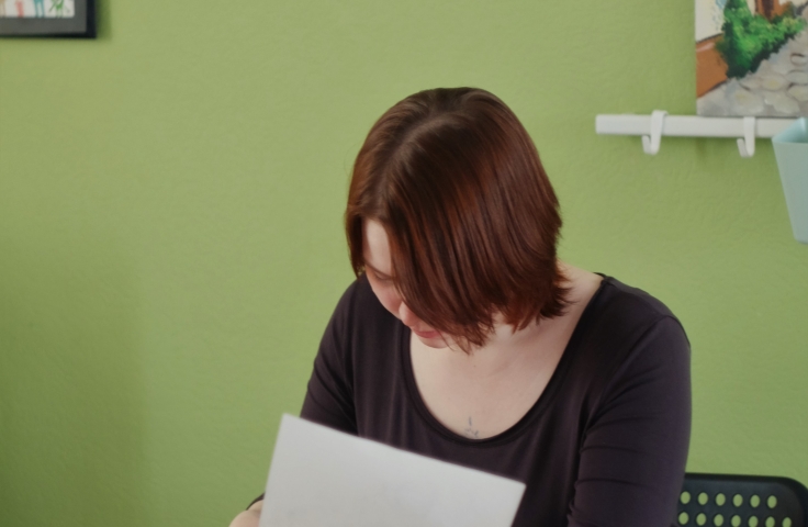 A woman sits at a desk reading a piece of paper