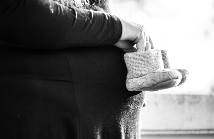 A pregnant person holding knitted baby booties