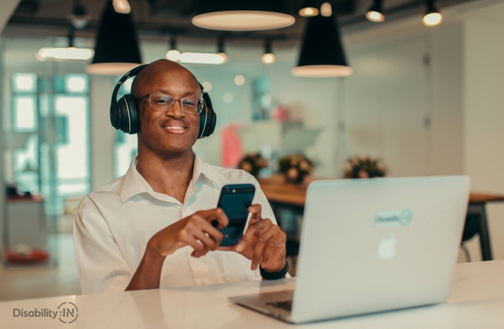 Man at his laptop with headphones on and a mobile phone in hand