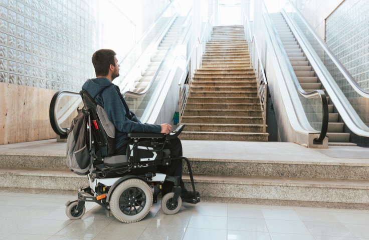 Wheelchair user at the base of a set of steps with no ramp or access 