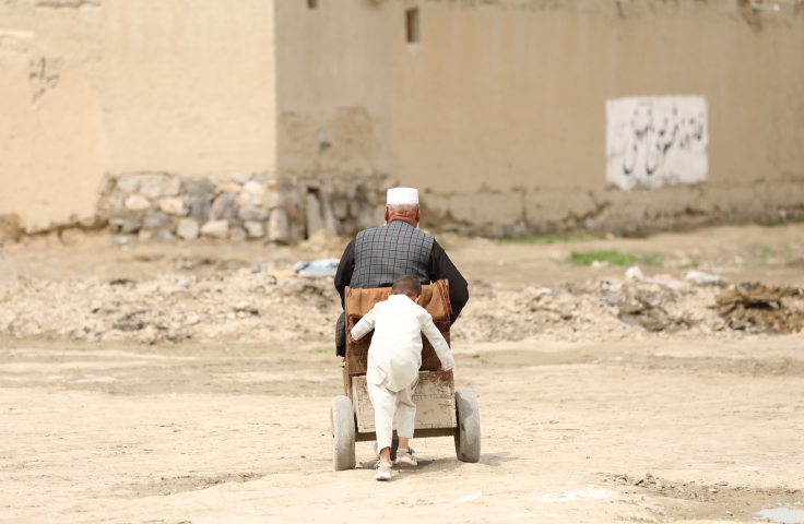 Man in white long sleeve shirt and white pants sitting on wheelchair being pushed by boy