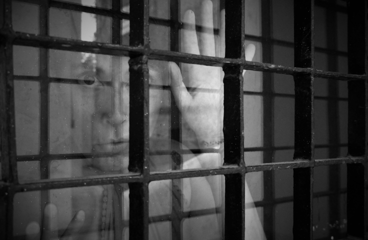 Grayscale photo of someone behind prison bars